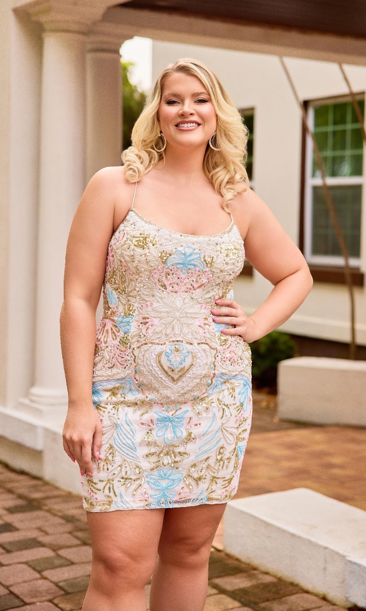 A woman smiles confidently outdoors, posing with one hand on her hip while wearing the stylish Primavera 14090 Plus-Size Short Lace-Up Hoco Dress.